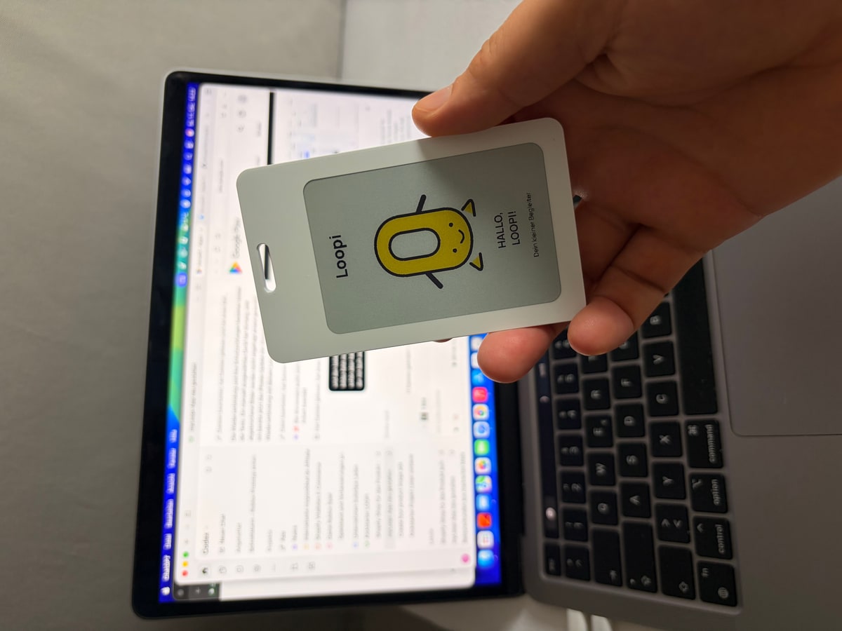 Original photograph of a white Loopi prototype held in a hand, showing the yellow Loopi Pet on its real E-Paper screen